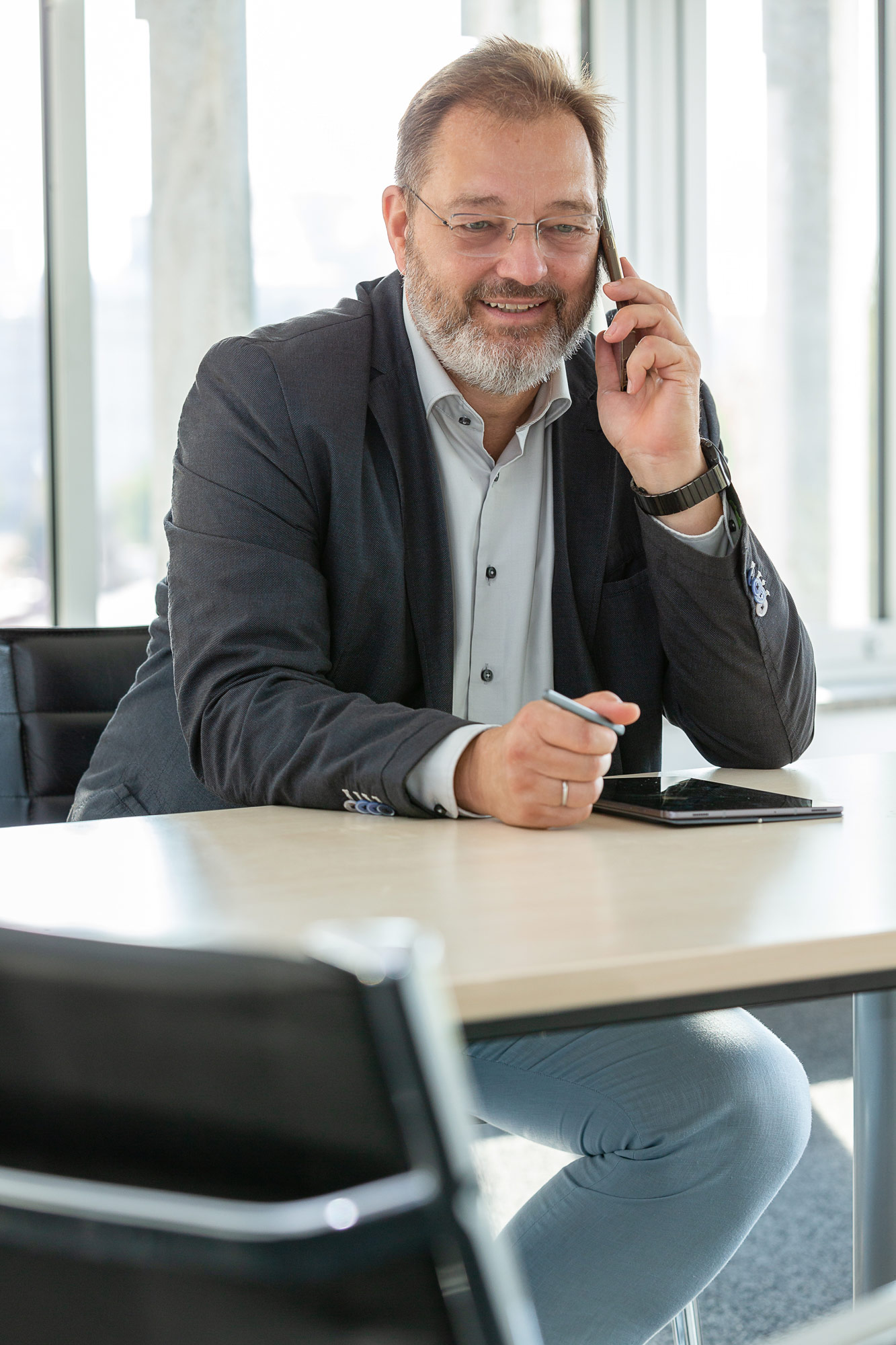 Ein älterer Mann mit grauem Bart lächelt freundlich beim Telefonieren am Schreibtisch